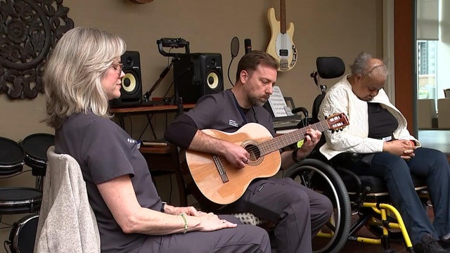 One person plays a guitar, two people have their eyes closed during the music and mindfulness group 
