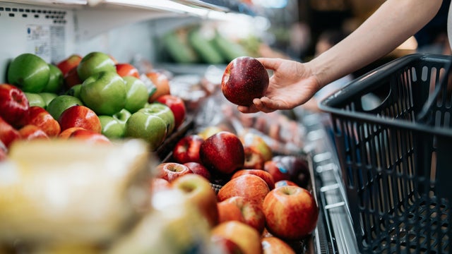 Cropped shot of young Asian woman choosing fresh organic fruits in supermarket. She is picking a red apple along the produce aisle. Routine grocery shopping. Healthy living and eating lifestyle 