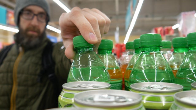 Close-up of a male buyer's hand taking a green plastic bottle of lemon soda from a supermarket shelf 